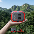 Hand holding a red and gray power adapter with mountainous landscape in the background